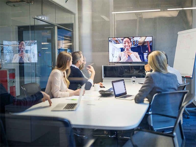 Employees sitting in a conference room(hybrid workplace) and meeting others virtually via video call